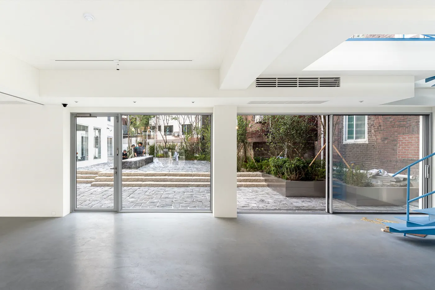 A bright empty hall with white walls and large glass doors opening onto a tree-lined courtyard