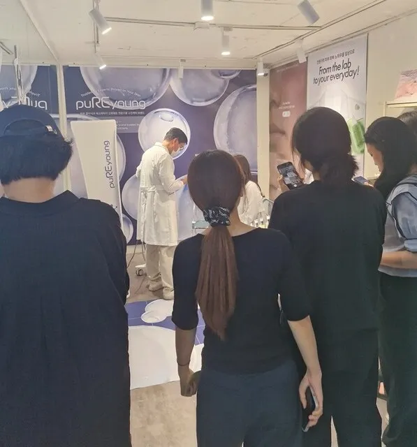 흰 가운을 입은 직원 앞에서 설명을 듣는 방문객