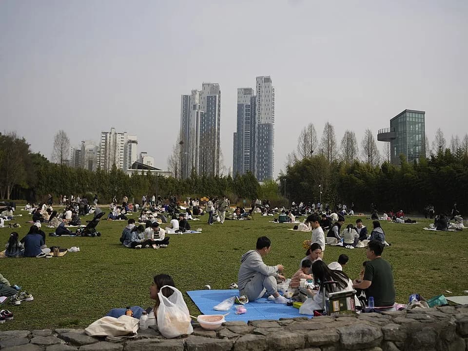 잔디밭에 돗자리를 펴고 봄나들이를 즐기는 서울숲 방문객들, 뒤로 고층 건물